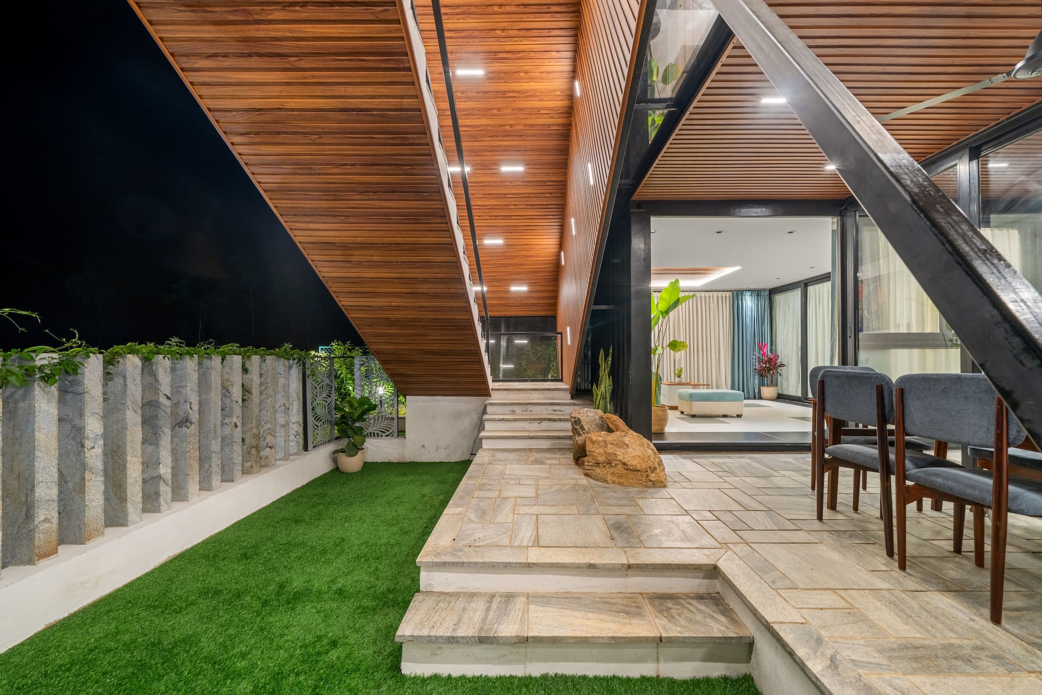Semi-open dining area with A-frame teak ceiling and geometric steel beams at night